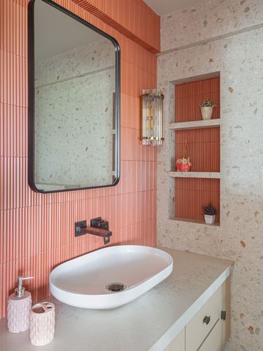 Bathroom vanity with coral fluted tile, terrazzo wall, black-framed mirror and oval white sink