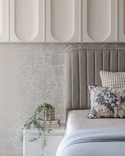 Beige channel-tufted headboard with patterned cushions against arched panel wall and floral wallpaper