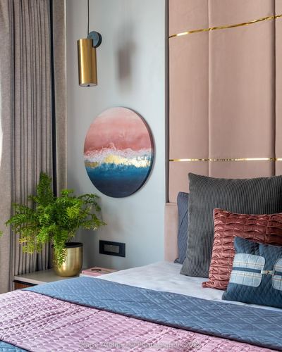 Bedroom corner with pink tufted headboard, brass pendant light, round ocean-themed art and fern