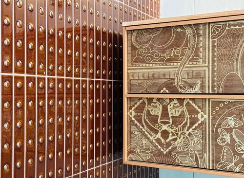 Close-up of studded maroon tile wall beside a wood vanity with hand-etched animal motif drawer fronts