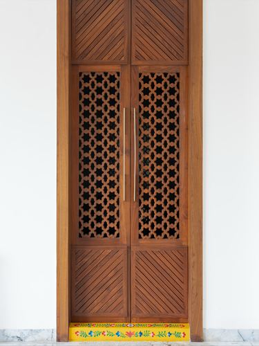 Tall wooden door with carved lattice panels and brass handles, painted threshold below