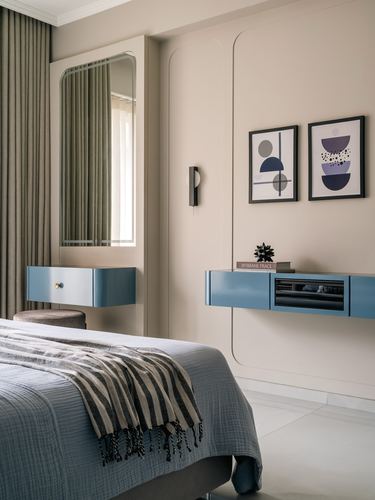 Beige bedroom with blue floating consoles, arched mirror, and framed abstract art above the bed