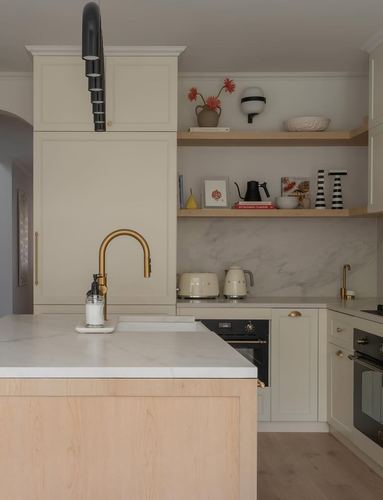 Cream kitchen with light wood island, marble-look backsplash, brass fixtures, and a black sculptural pendant light