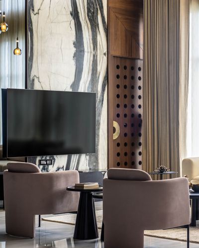 Living room with book-matched marble wall, perforated wood panel, and mauve armchairs around a round table
