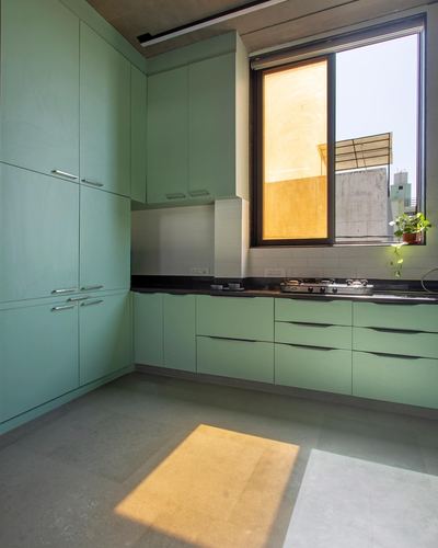 Sage green L-shaped kitchen with black countertop and sunlight streaming through a large window