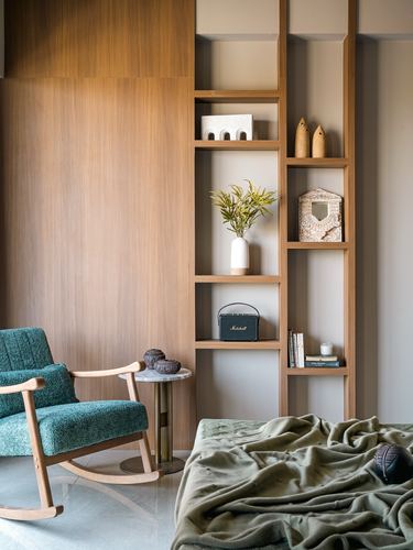 Green rocking chair beside wooden display niches with decor and a bed with olive throw
