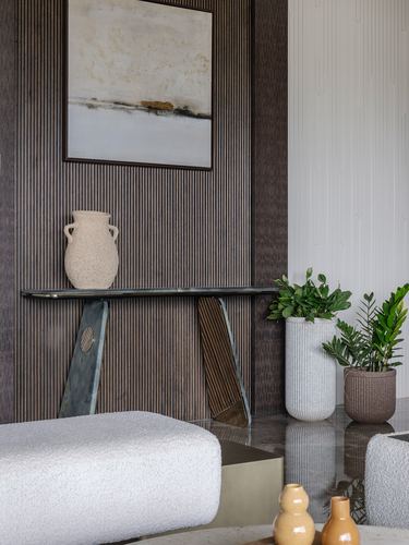 Console table with vase and artwork against fluted wood wall beside plants and ottoman