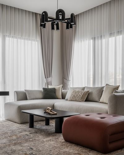 Neutral living room with grey sectional, black coffee table, rust ottoman, and tall sheer curtains