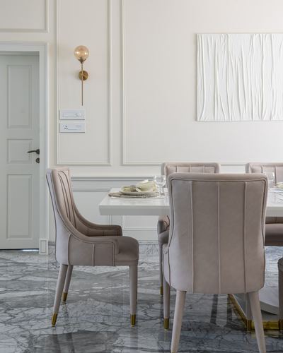 Blush velvet dining chairs around white table on marble floor, panelled white wall behind