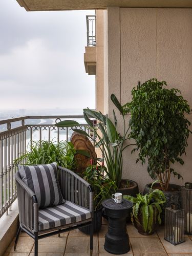 High-rise balcony with wicker chair, striped cushion, potted plants, and hazy city-water view