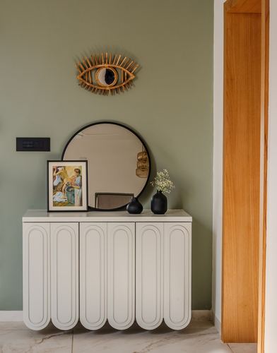 Sage green foyer wall with round mirror, rattan eye art, and scalloped white sideboard