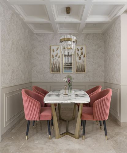 Dining nook with pink velvet chairs around marble table under crystal chandelier and coffered ceiling