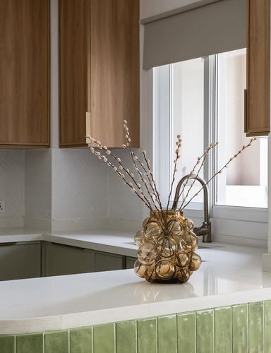 Kitchen counter detail with amber glass vase, wood cabinets, and green tiled island edge near window