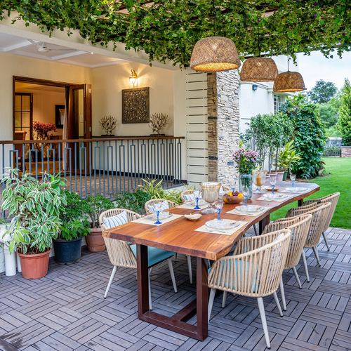 Covered terrace dining table under vine-covered pergola with woven pendant lights and garden view