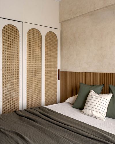 Bedroom with arched cane wardrobe doors and fluted wood headboard against textured plaster wall