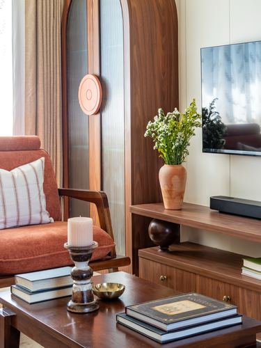 Living room corner with arched wooden wardrobe, terracotta vase, and rust sofa near tv console