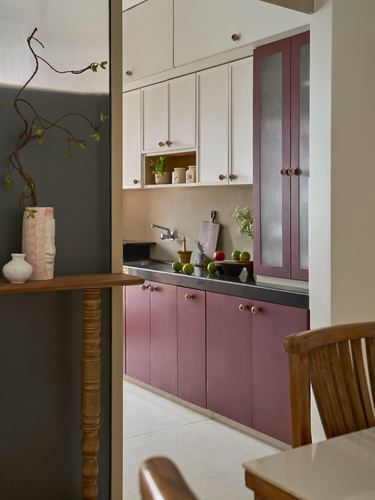 View through dark doorway into mauve and white kitchen with black countertop