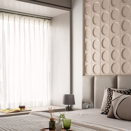 Bedroom with textured circular wall panelling above upholstered headboard beside sheer-curtained window