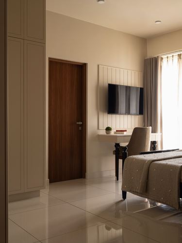 Beige bedroom with wood-veneer door, fluted panel wall with mounted TV, and console desk chair