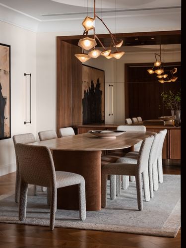 Elegant dining room with oval walnut table, boucle chairs, and sculptural brass chandelier