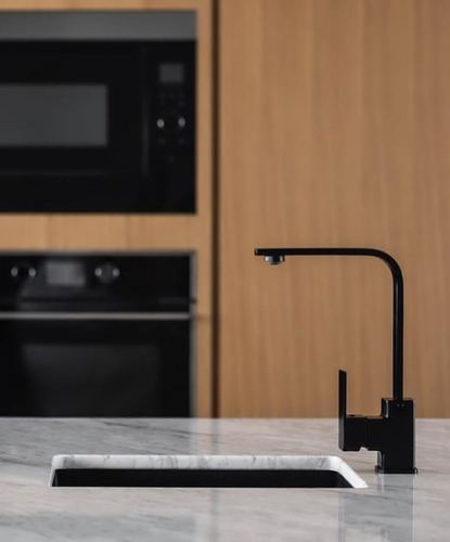 Close-up of black faucet and sink on stone counter with wood-paneled kitchen background
