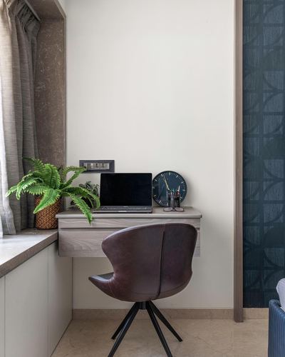 Wall-mounted desk with laptop and clock beside window, brown leather chair in front