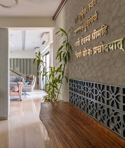 Foyer wall with gold Sanskrit mantra lettering above a jali panel and wooden bench