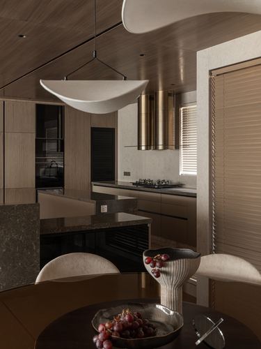 Warm-toned kitchen with fluted wood cabinetry, brass hood, stone island, and sculptural pendant light