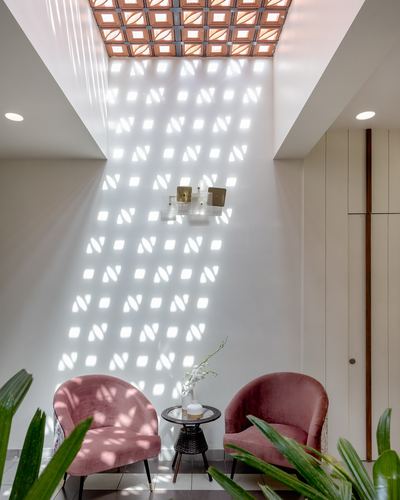 Double-height nook with terracotta jali skylight casting patterned light over pink velvet chairs