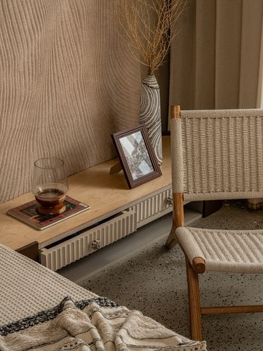 Wooden console with vase, framed photo and glass beside a woven chair on terrazzo floor