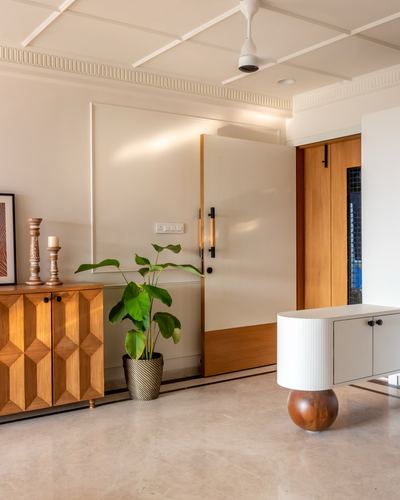 Entryway with fluted wooden door, geometric wood sideboard, and round white cabinet on marble floor