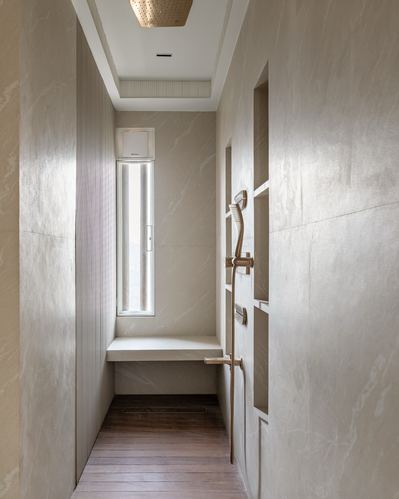 Narrow marble-tiled shower with brass fixtures, recessed niches, and a window seat at the end