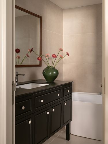 Bathroom with dark wood vanity, mirror, green vase of red flowers, and freestanding tub beyond