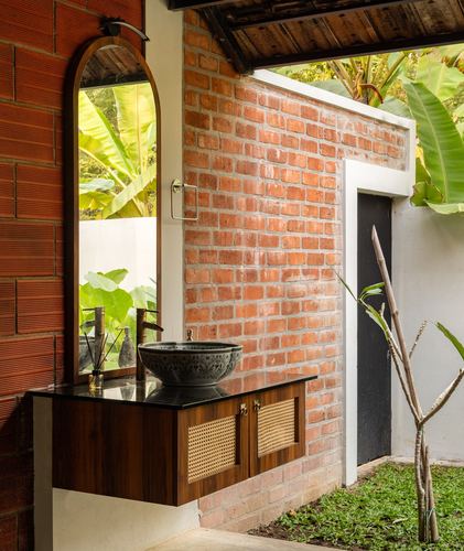 Outdoor bathroom vanity with round stone sink against exposed brick wall and arched mirror