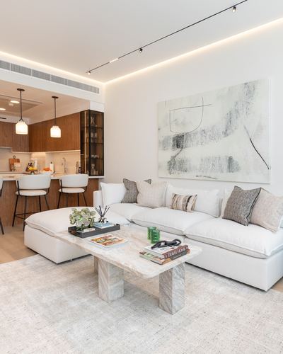 Open-plan living room with white sectional sofa, marble coffee table, and wood kitchen beyond