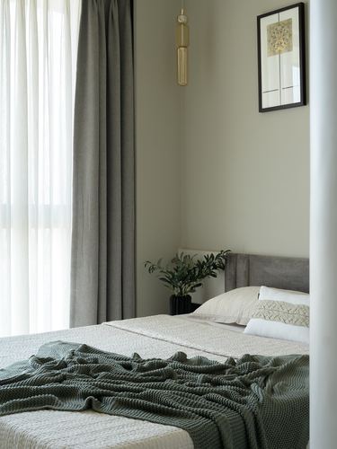 Neutral bedroom with grey headboard, green knit throw, sheer curtains and hanging pendant light