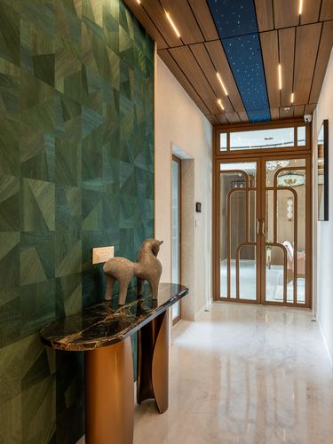 Entry corridor with faceted green wood wall, marble console, and brass-framed glass door beyond