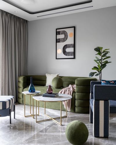 Living room with olive green tufted sofa, marble nesting tables, and framed graphic art on grey wall