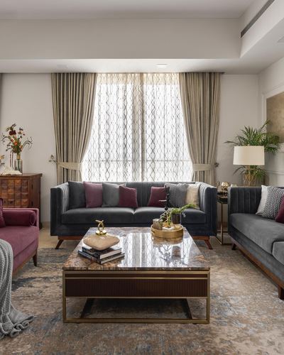 Formal living room with grey channel-tufted sofas, burgundy armchair, and marble coffee table before curtained window