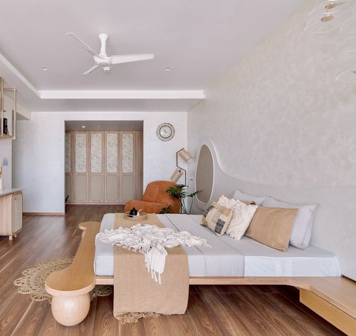 Bedroom with curved wooden bed, organic headboard, terracotta armchair and wardrobe alcove beyond