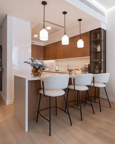 Kitchen island with three grey stools under three globe pendant lights, wood cabinetry behind