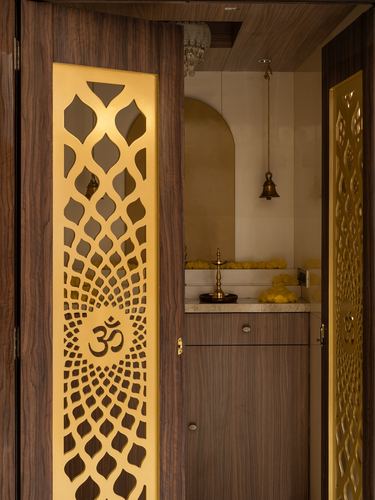 Wooden door with golden om jali screen opening into a marble-countered pooja room with hanging bell