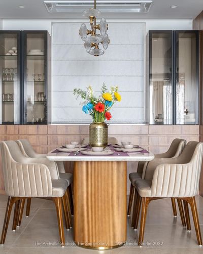 Dining table with marble top, fluted gold pedestal, flowers, flanked by glass cabinets