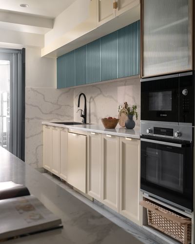 Galley kitchen with cream cabinetry, marble backsplash, teal fluted overhead unit and built-in ovens