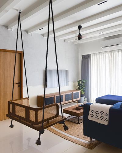 Living room with hanging cane swing, wooden console, and navy sofa under exposed beam ceiling