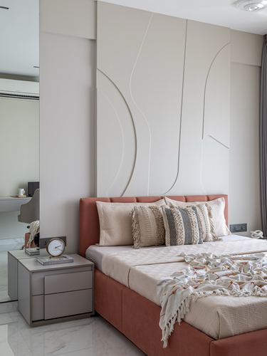 Bedroom with terracotta upholstered bed against a sculpted white wall panel and stone flooring