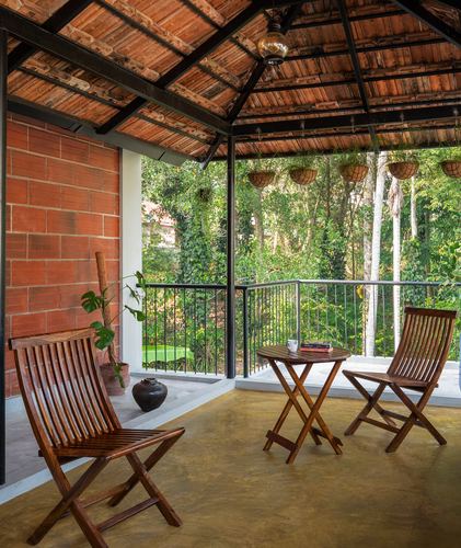 Covered verandah with wooden folding chairs, brick wall, and terracotta roof overlooking forest