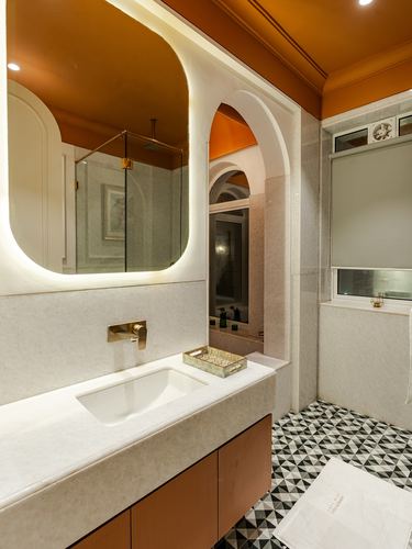 Bathroom vanity with backlit arched mirror, brass fittings, and geometric black-and-white tile floor