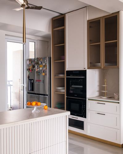 Cream kitchen with ribbed glass cabinets, built-in ovens, marble counters, and an island with oranges
