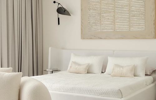 Cream bedroom with quilted white bedding, black wall sconce, and a textured framed panel above the headboard